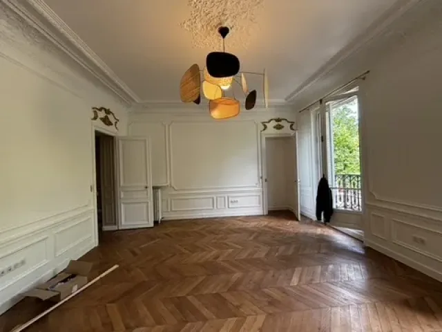 Séjour rénové : moulures et corniches conservées, parquet à bâtons rompus remis en état, suspension contemporaine à disques.