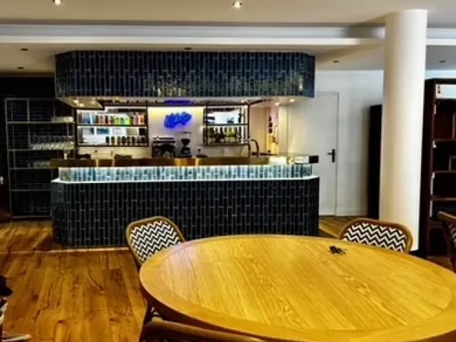 Après travaux : salle livrée, comptoir habillé de zelliges bleu nuit, étagères à bouteilles et table ronde en bois.