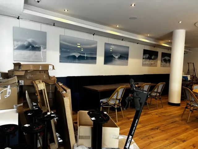 Après travaux : la salle livrée, cadres photographiques au mur, banquette et chaises le long de la colonne.