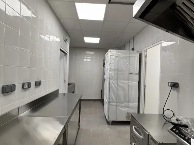 Après travaux : cuisine livrée — plan de travail en inox sur toute la longueur, armoire réfrigérée et hotte.