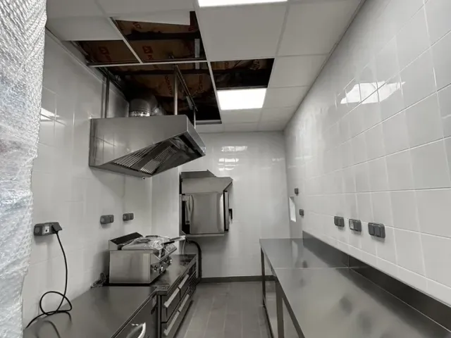 Après travaux : ligne de cuisson sous la hotte inox, crédence carrelée, plafond technique encore ouvert au-dessus.