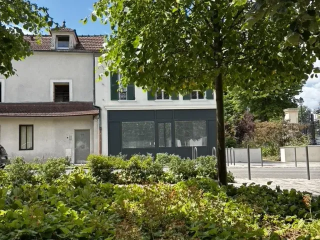 Avant travaux : abords du local vus depuis la rue, haie et bâtiment voisin.