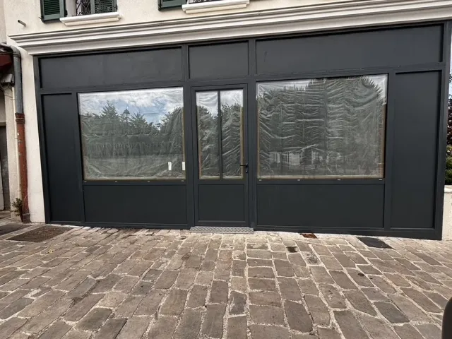 Avant travaux : devanture existante fermée, vitrines occultées par un film de protection, parvis pavé.
