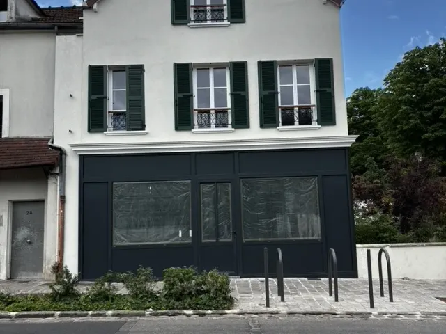 Avant travaux : le bâtiment depuis la rue, façade claire à volets et devanture sombre en rez-de-chaussée.