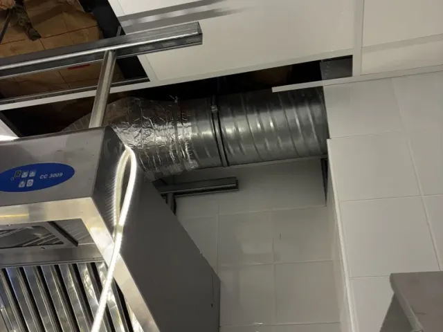 Chantier : hotte d'extraction en inox posée contre le mur carrelé de la cuisine.