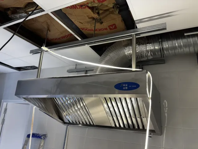 Chantier : hotte et gaine d'extraction raccordées, ossature du plafond suspendu encore ouverte.