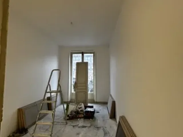 Pièce en cours de travaux, murs remis en peinture, radiateurs déposés et posés au sol le long des cloisons.