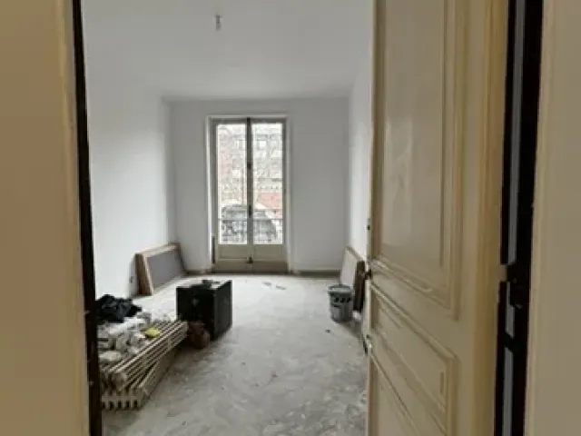 Pièce vidée en cours de chantier, vue depuis le couloir à travers une porte à panneaux conservée.