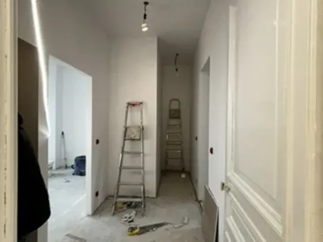 Couloir en travaux, spots sur rail déjà posés au plafond, escabeau et outillage au sol.
