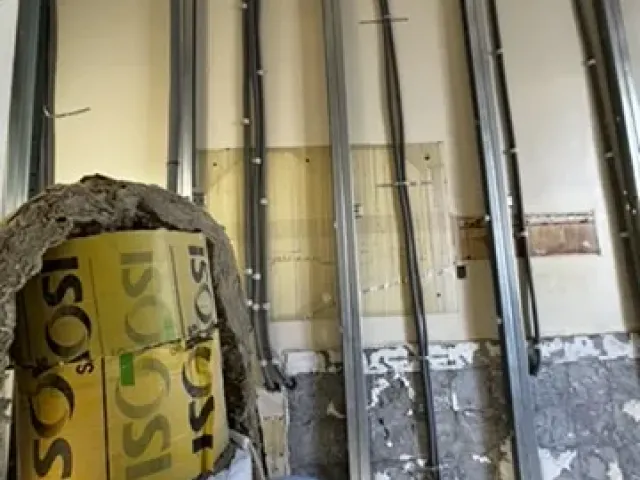 Ossature métallique d’un doublage isolé, attentes électriques en place devant un mur décroûté.